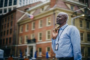 Smiling man in a blue shirt stands outside in front of a historic brick building, embodying the future of technology governance.
