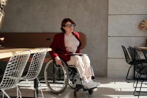 A woman in a wheelchair wearing a red blazer sits at a table in a bright, modern room, reflecting a commitment to belonging in inclusive spaces.