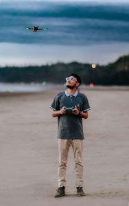 Man flying a drone on a sandy beach, looking up at it with commitment as he holds the remote control in his hands.