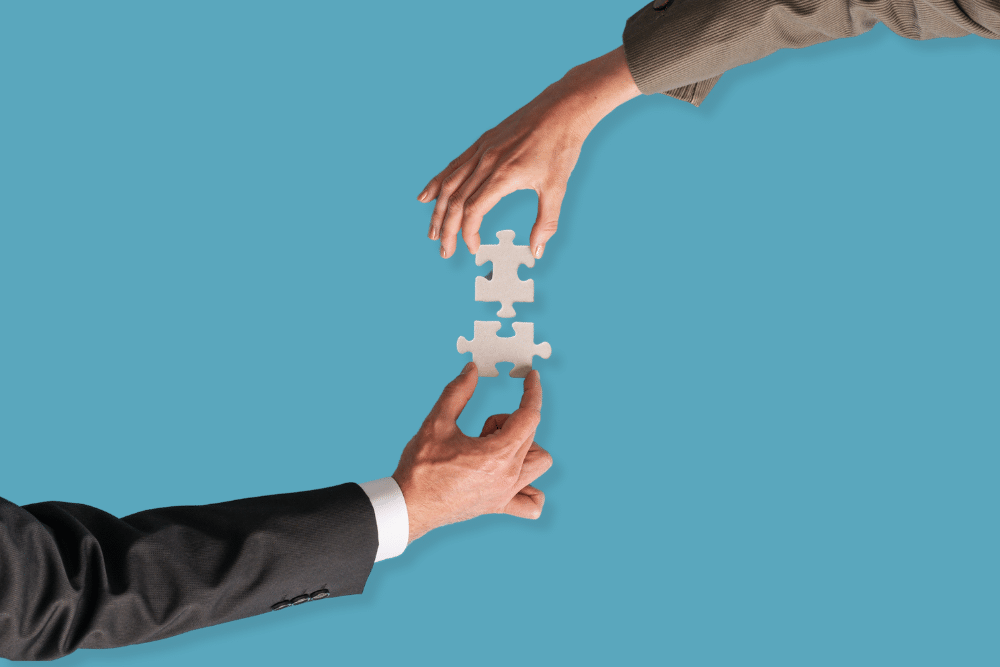 Two businesspeople's hands holding puzzle pieces coming together