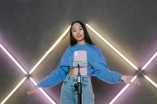 Woman in a blue top dances in front of a smartphone and neon lights shaped like X’s, capturing the spirit of tech policy in action.