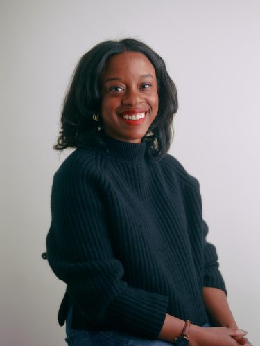 Nicole Allred, a woman with shoulder-length dark hair, wears a black sweater and smiles against a plain light background.