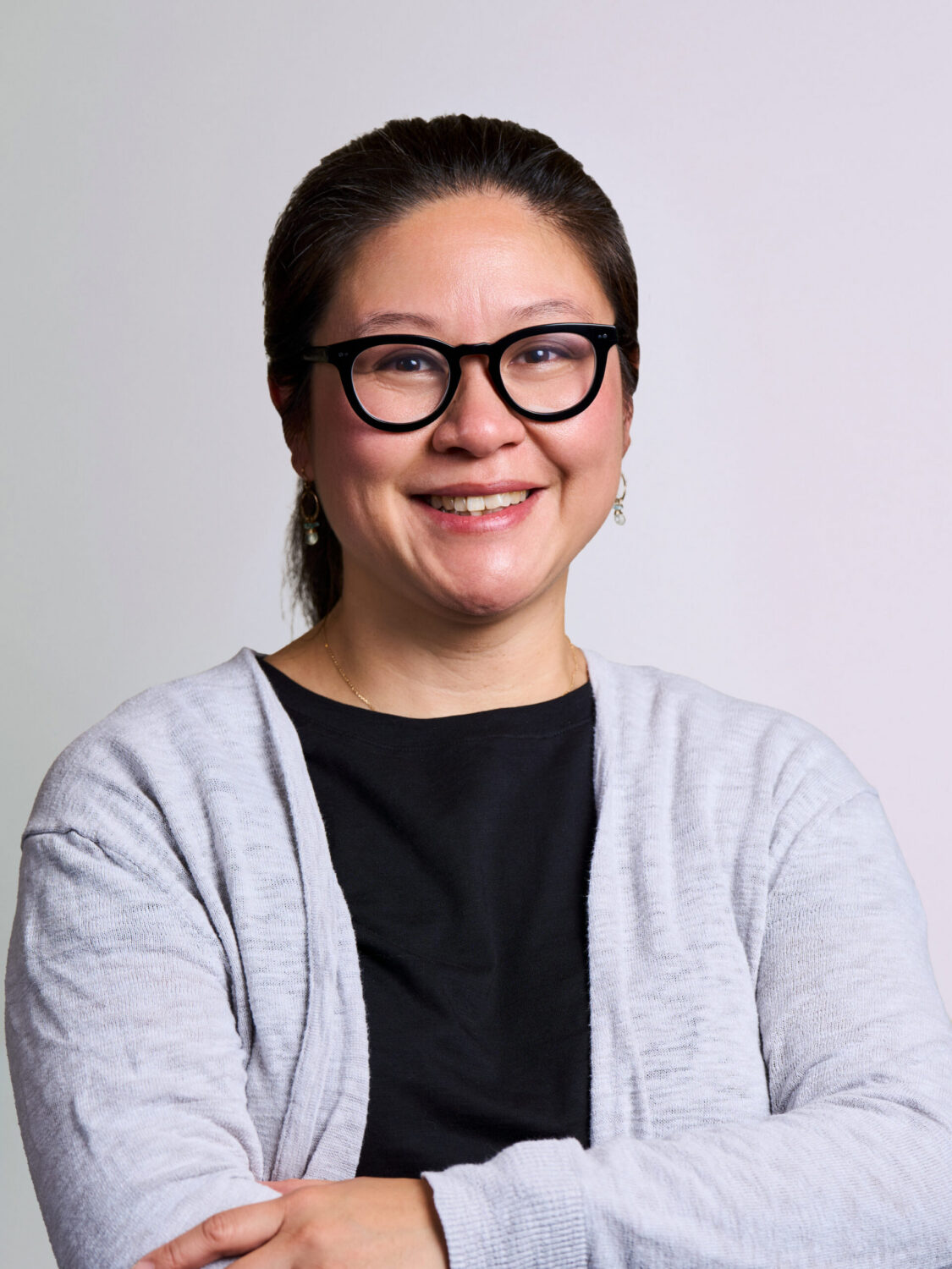 Portrait of a smiling woman with dark hair wearing black-rimmed glasses and a grey cardigan.