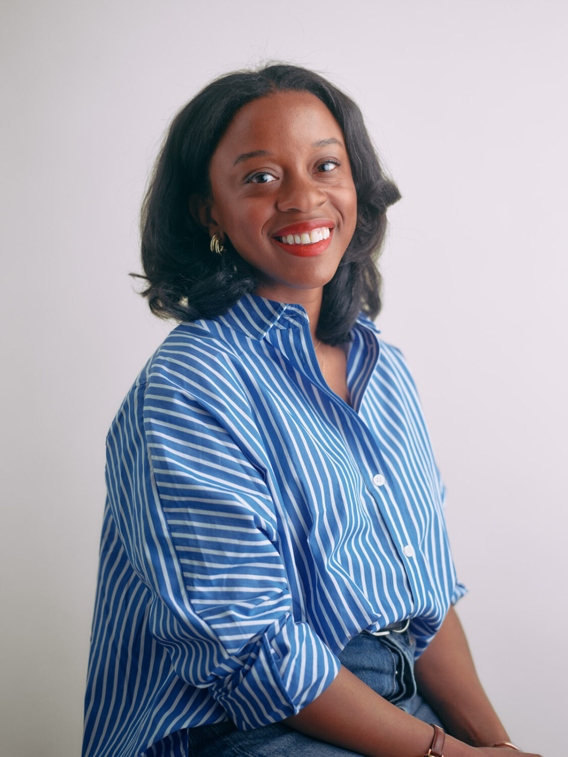 Nicole Allred, a smiling woman in a blue striped shirt, is seated against a plain white background.