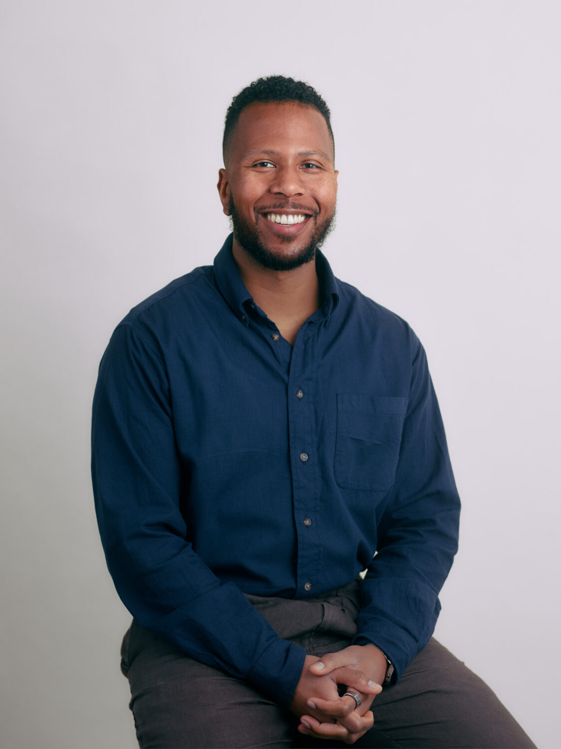 A smiling man in a blue shirt sits against a plain background.