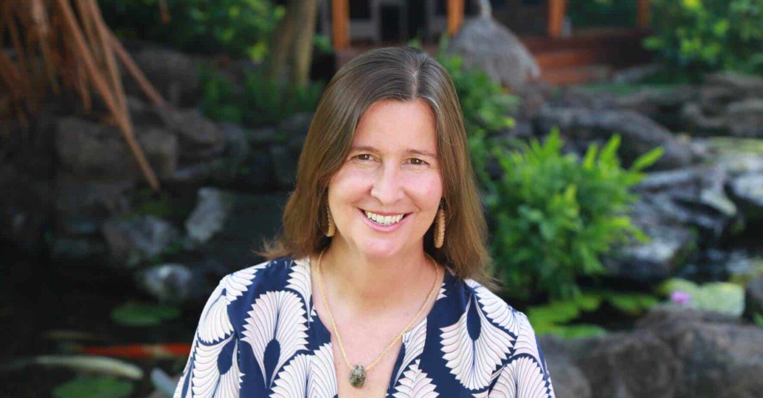 A smiling woman in a patterned blouse, seated in a lush garden with greenery and rocks, embodies the harmony of humanity and nature, reminding us of the seamless integration that technology and AI can bring to our everyday lives.