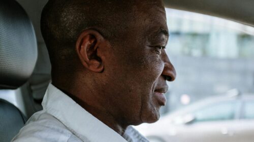 Man driving a car, wearing a white shirt and seatbelt, looking forward.