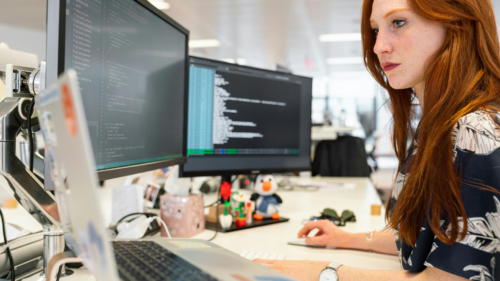 Person working on multiple computer screens displaying code in an office setting.