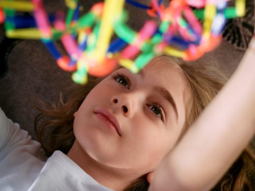 A child lying down in Nebraska, looking intently at a colorful geometric construction toy above them