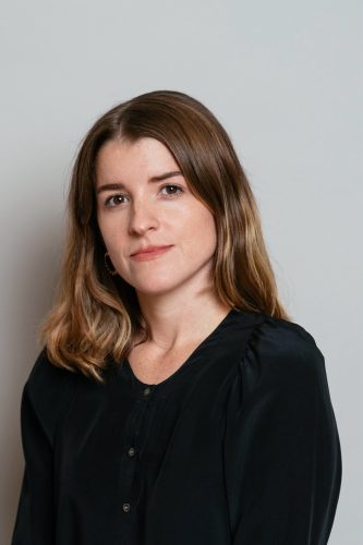 Woman with shoulder-length brown hair wearing a black blouse, looking at the camera with a neutral expression.