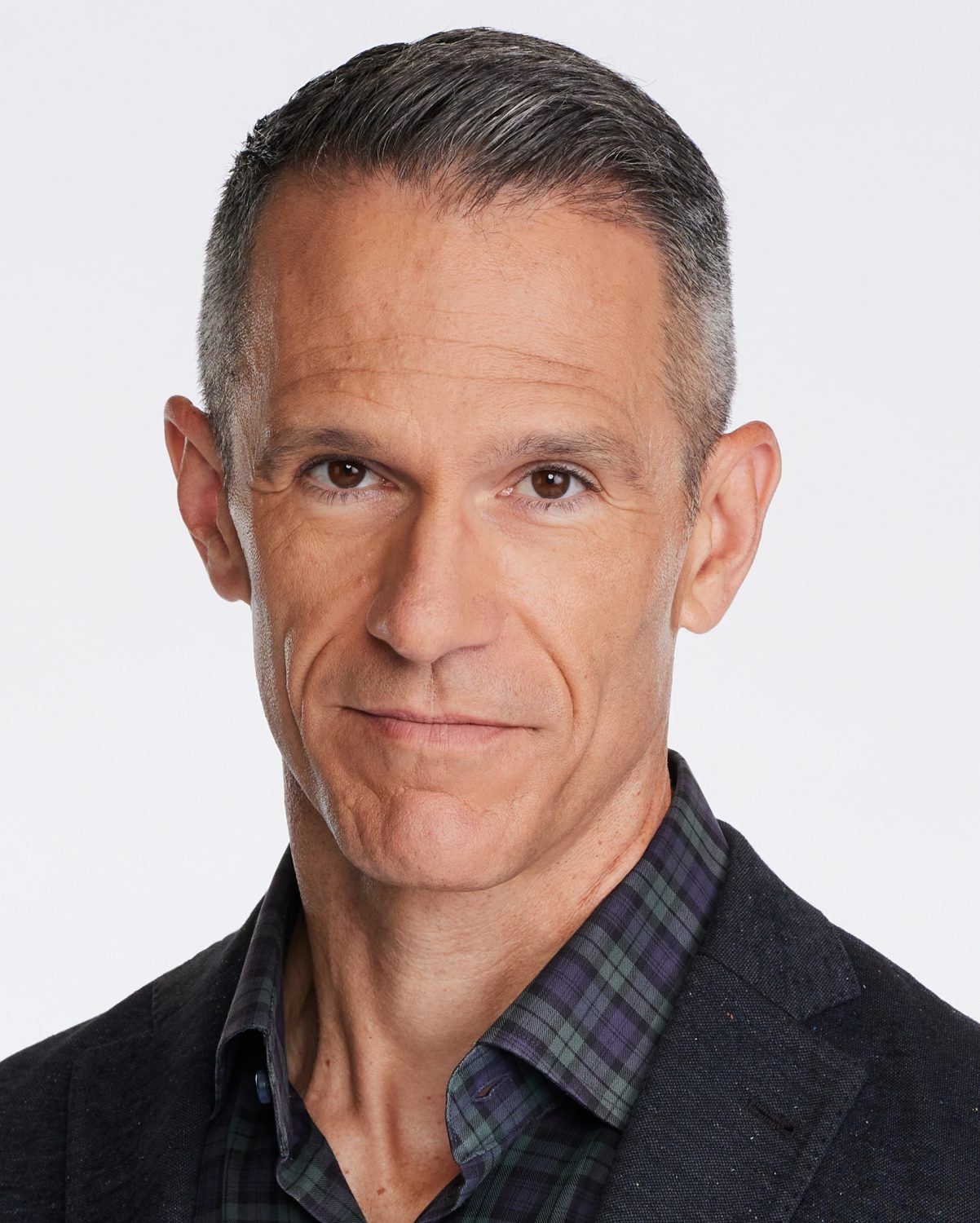 Middle-aged man with short gray hair, wearing a dark blazer and plaid shirt, looking at the camera.