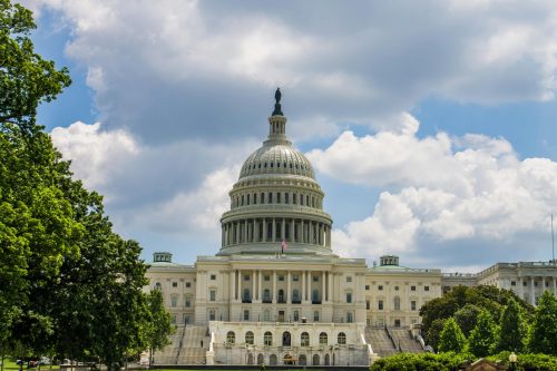 The U.S. Capitol building in Washington, D.C. under a partly cloudy sky, framed by trees—a symbolic backdrop as debates on States’ Right to Govern AI gain momentum.