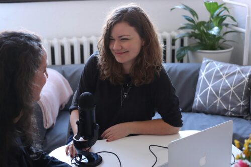 Two women sit at a table with a microphone and laptop, smiling and talking in a cozy room about independent journalism and the impact of funding from organizations like the Omidyar Network.
