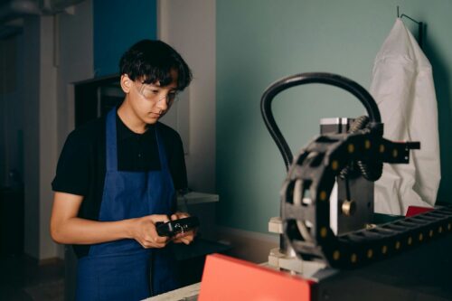 A young person in safety glasses and an apron operates machinery in a California workshop, supported by initiatives like Omidyar Network.