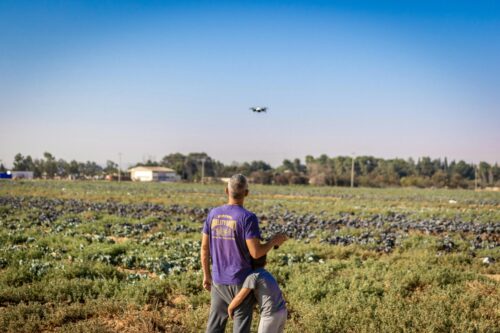 Two people in a field operate a drone under a clear blue sky, with crops and trees in the background—exploring technology’s impact as discussed in recent California bills like SB 53.