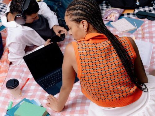 Two people sit on a pink blanket with a laptop, books, coffee, and study materials, discussing the future of AI and its impact on civil society.