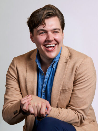 Man smiling with brown jacket and blue shirt