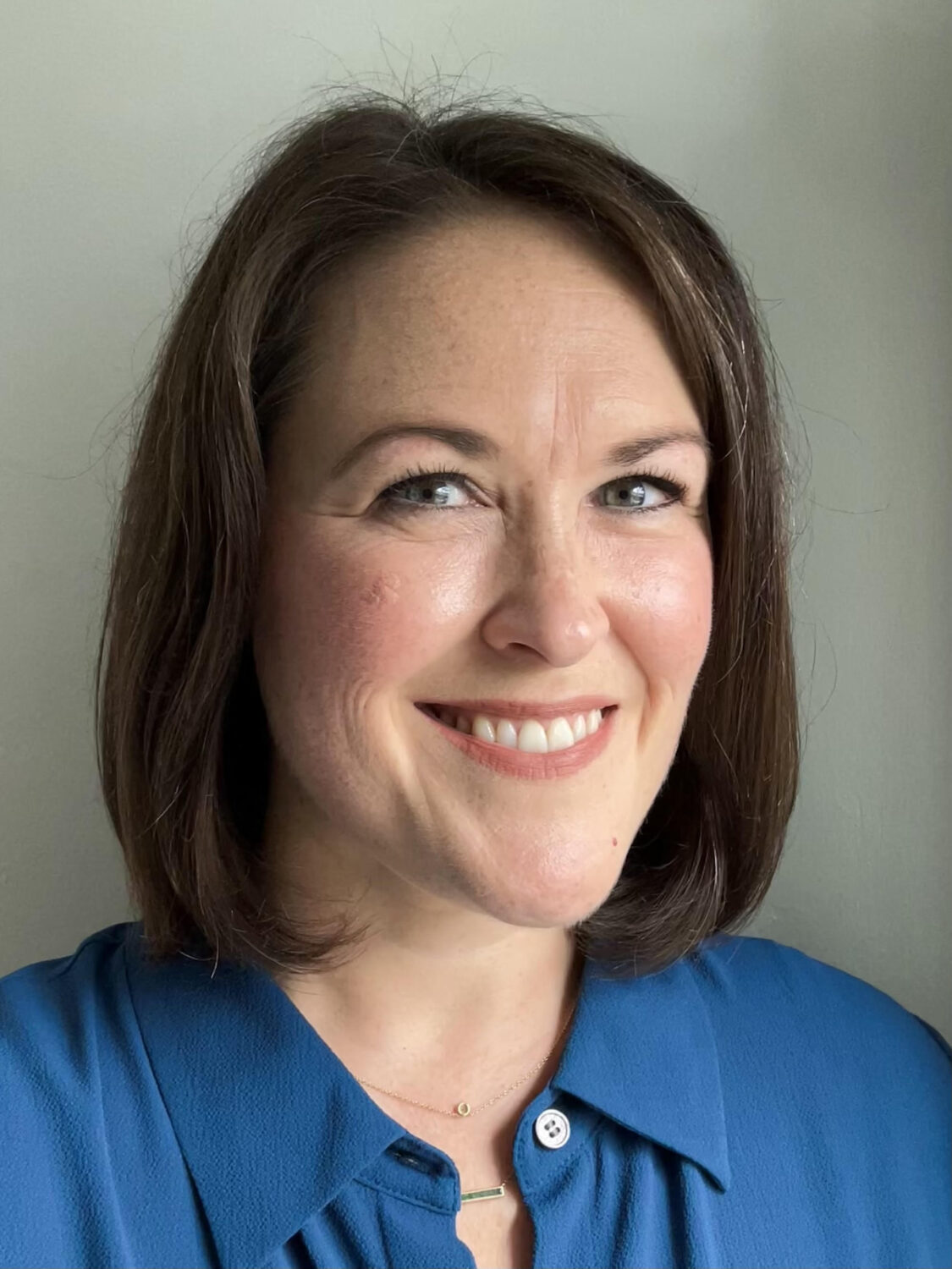 Smiling woman with straight brown hair wearing a blue shirt, resembling Issie Lapowsky, faces the camera against a plain background.